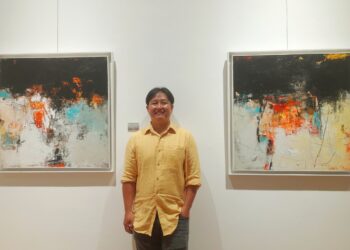 Pelukis abstrak asal Bali, Tien Hong berpose diantara dua karyanya. -Balitopik.com