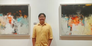 Pelukis abstrak asal Bali, Tien Hong berpose diantara dua karyanya. -Balitopik.com