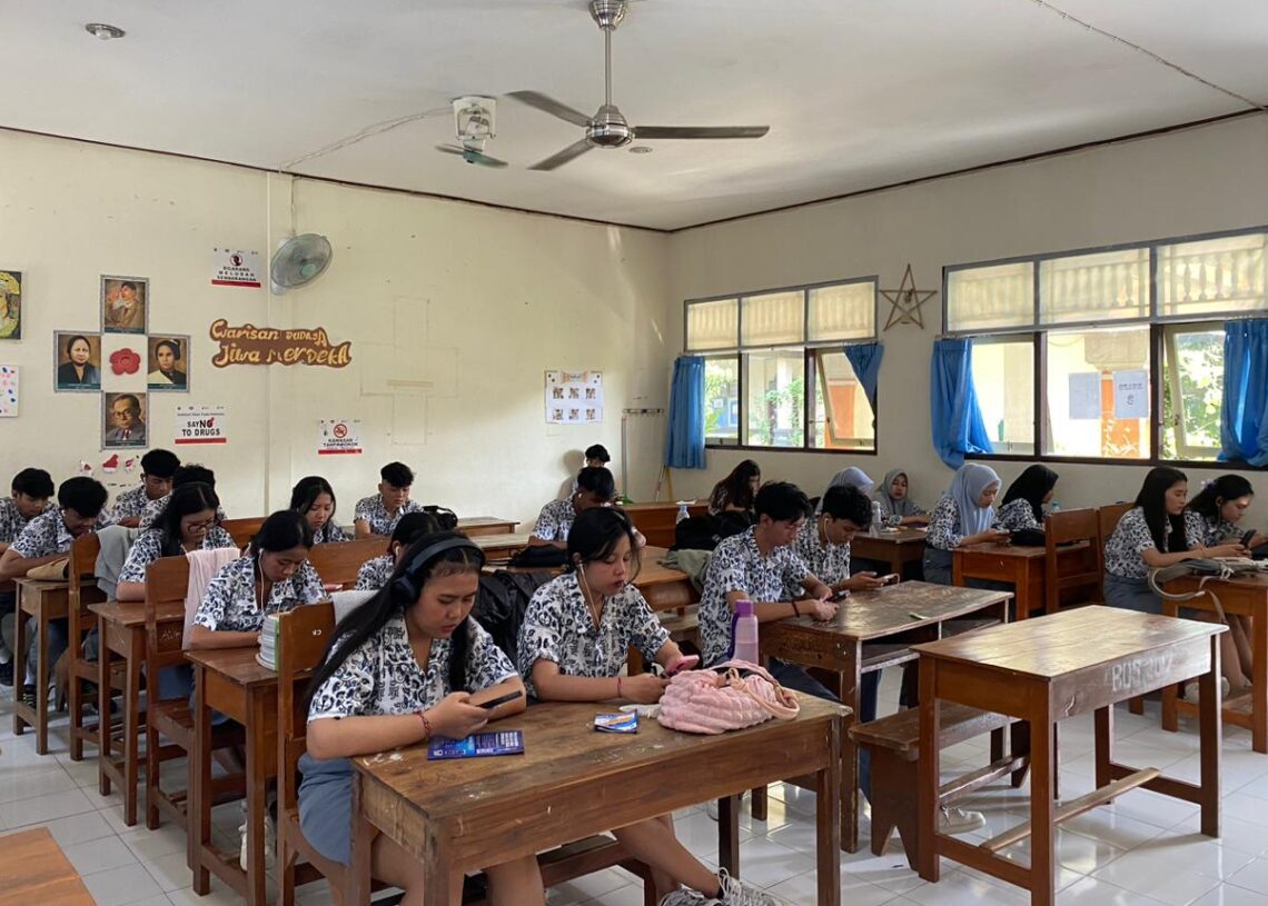 Siswa SMK PGRI 2 Denpasar mengerjakan tes bahasa Inggris HeadWay melalui handphone di dalam kelas.
