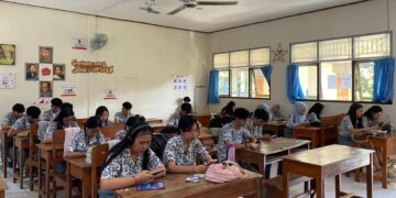 Siswa SMK PGRI 2 Denpasar mengerjakan tes bahasa Inggris HeadWay melalui handphone di dalam kelas.